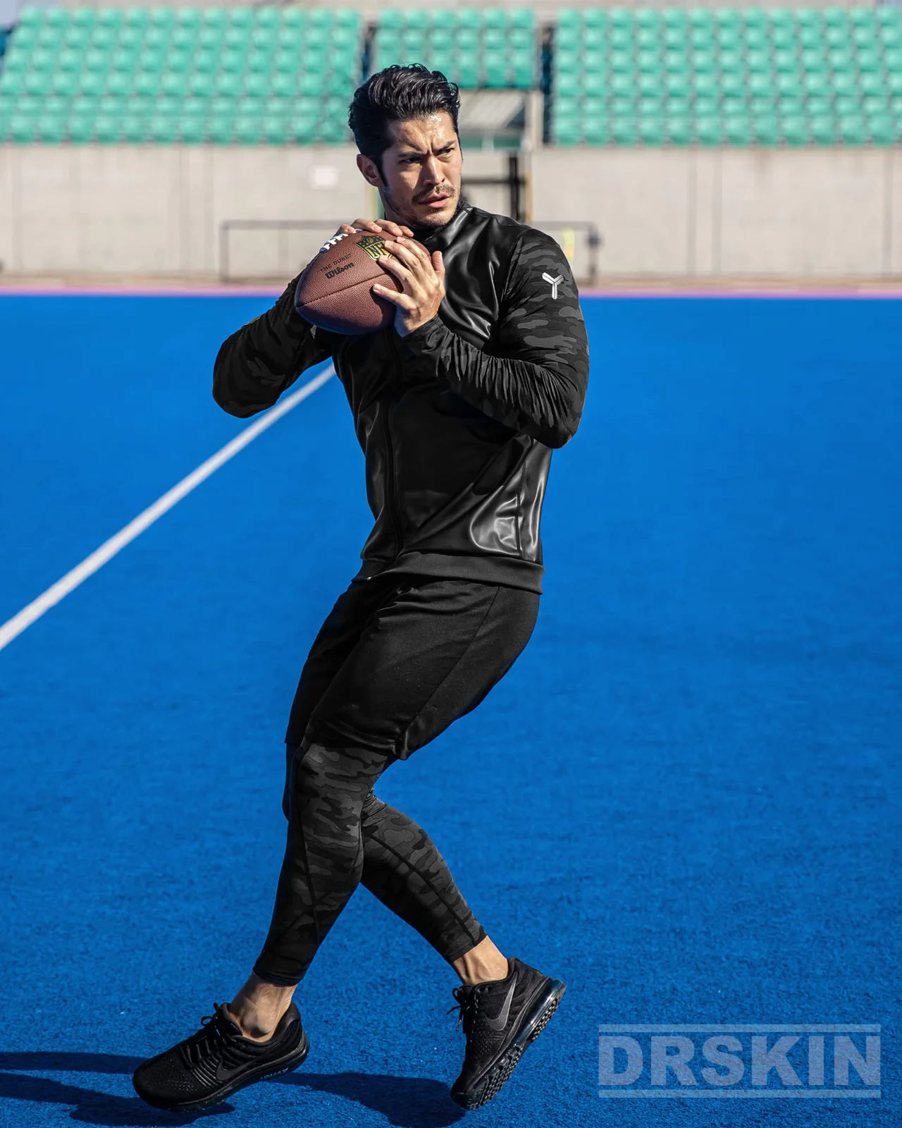 Black compression tights on a blue running track, the athlete leaning into a resistance-band sprint